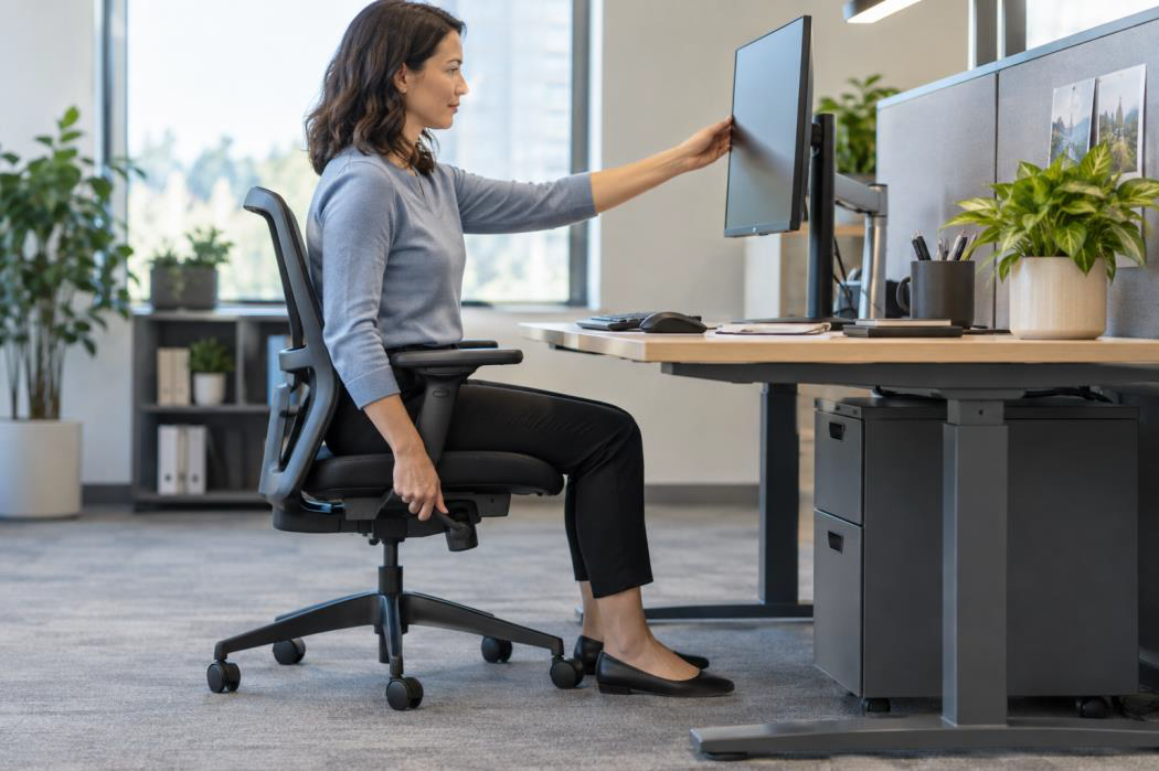 Employee adjusting an ergonomic workstation and monitor